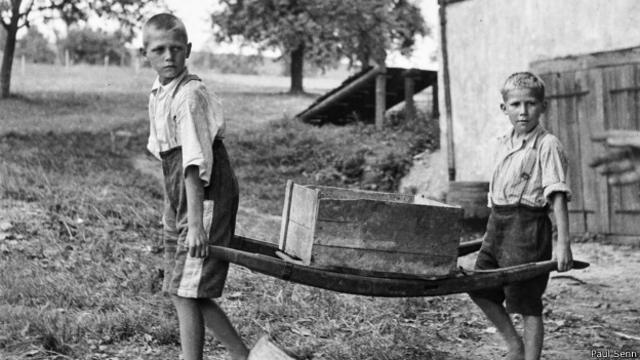 Dos niños sin zapatos cargan una carretilla