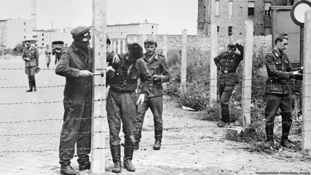 14 अगस्त 1961 के पूर्वी जर्मनी की पीपल्स नेशनल ऑर्मी के कर्मचारी बर्लिन की दीवार के निर्माण से पहले कंटीली तार लगा रहे हैं.