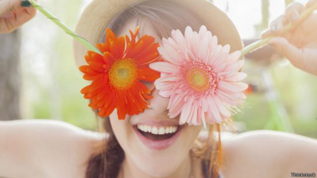 Mujer sonriendo y cubriendo los ojos con flores