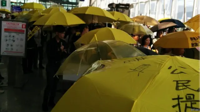 支持学联的数十人手持黄雨伞,在学联代表登机的柜台附近聚集和唱歌。