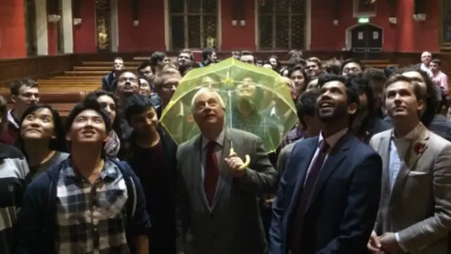 前港督彭定康2014年10月底在牛津大學一次活動中,撐起由學生送上的象徵香港「佔中」運動的黃色雨傘。 (資料圖片)