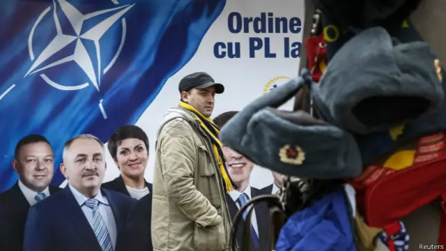 Человек на фоне плаката НАТО и ушанки