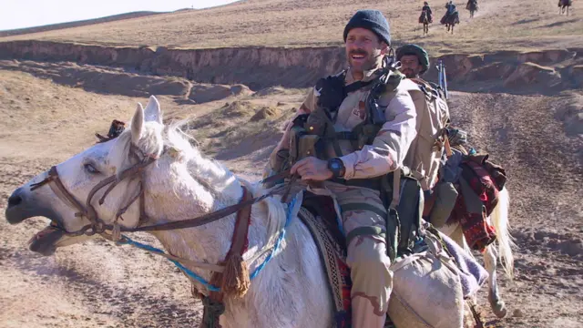 امریکایی عملیاتو غړی بارټ ډېکر دوستم سره راوخوت او امریکايي بم ویشتونکو ته یې د طالبانو موقعیت په اړه مالومات ورکوي، د ۲۰۰۱ کال نومبر میاشت.