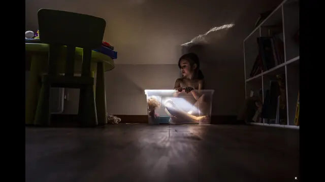 Пластик қути ичидаги қўғирочоқ билан суҳбатлашаётган қиз сурати учун фотограф К мукофотланди.