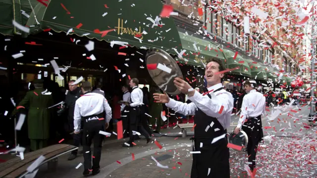 在伦敦著名的哈罗兹百货商店门外，店员抛撒彩纸条，为排队的购物者们助兴。