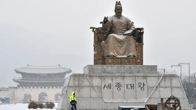 جنوبی کوریا کے دارالحکومت سیول میں ایک پولیس اہلکار برفباری کے دوران سیجونگ بادشاہ کے مجسمے کے قریب کھڑا ہے۔ 
