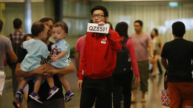 سنگاپور کے چانگی ہوائی اڈے پر ایئر ایشیا کا ایک اہلکار فضائی کپمنی کے لاپتہ طیارے کے مسافروں کے لواحقین کو متوجہ کرنے کے لیے پرواز کے نمبر QZ8501 والا کارڈ اٹھائے کھڑا ہے۔