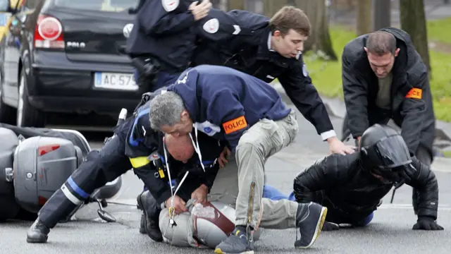 پولیس اہلکار سکوٹر پر افراد دو افراد کو زبردستی کوشر سپر مارکیٹ جانب سے روک رہے ہیں۔ 