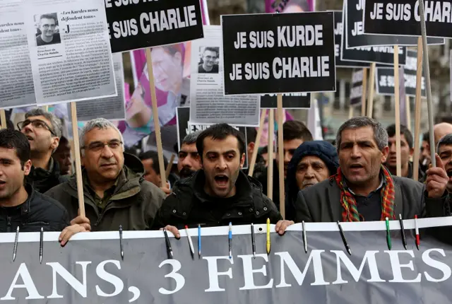جمعی از کرد‌های پاریس روی پلاکارد نوشته‌اند 'من شارلی ابدو هستم، من کرد هستم'. همچنین روی پلاکارد (پایین) نوشته شده 'سه سال پیش سکینه، فیدان و لیلا [سه فعال کرد] کشته شدند و حالا شارلی ابدو'