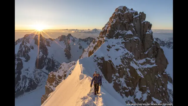 Los montañeros Ally Swinton y Brooke Kerrigan en la cresta de la cima de la Aiguille Verte con el Grand Rocheuse detrás, al amanecer.
