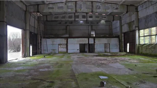 А це - закинуте промислове приміщення, бетонна підлога якого обросла мохом. Сильний вітер хитає масивні ворота - й іржаві завіси зловісно скриплять. 