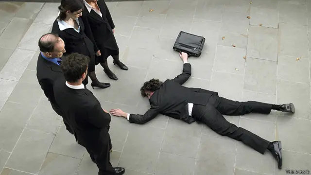 Бизнесмен лежит на асфальте, окруженный коллегами