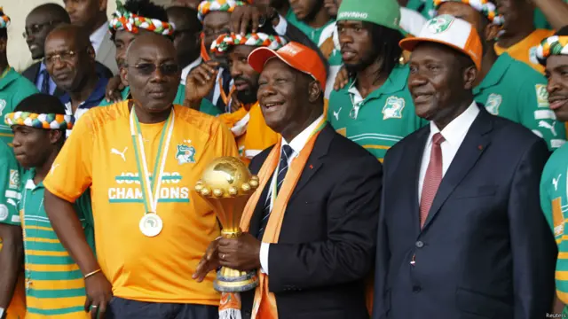 Le président Alassane Ouattara pose, trophée en main avec l'équipe ivoirienne, le président de la Fédération ivoirienne de football (FIF) Augustin Sidy Diallo (2nd G) et le premier ministre Daniel Kablan Duncan (2nd D), à l'aéroport International Felix Houphouet Boigny, à Abidjan le 9 février 2015