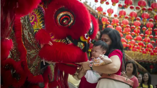 名女子怀抱小孩观看舞狮表演