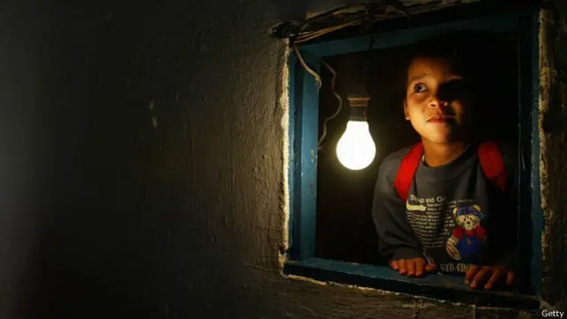 Un niño mira por una ventana con una bombilla encendida