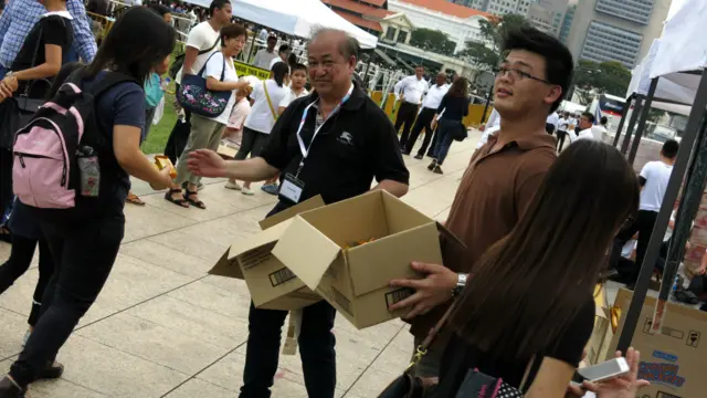 志愿者向排队等候吊唁者派发饼干(BBC中文网图片26/3/2015)