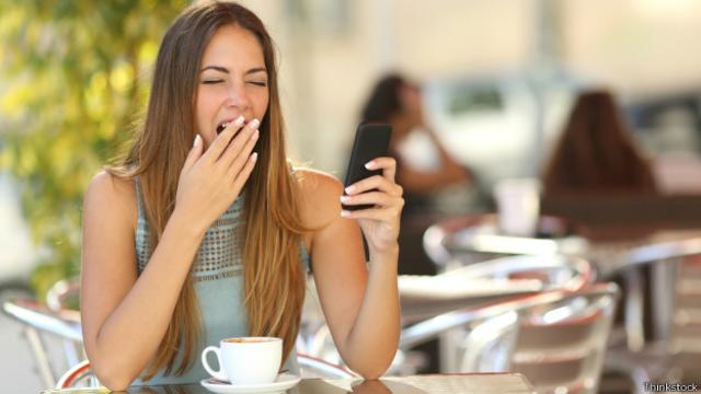 Mujer bostezando mientras ve su celular 