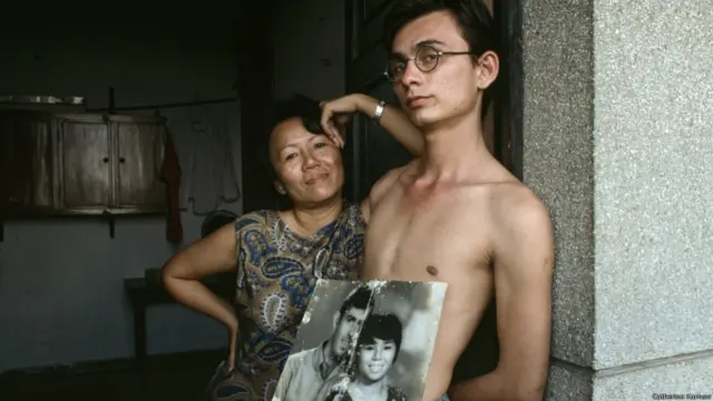 CẬU BÉ LAI MỸ VÀ MẸ, 1990. Jim và người mẹ Việt Nam của mình cầm một bức ảnh của bà với người chồng Mỹ, cha của Jim. Họ là một gia đình cho đến khi người cha quyết định trở về nhà với gia đình cũ mà ông ta đã có nhưng luôn giấu diếm. 