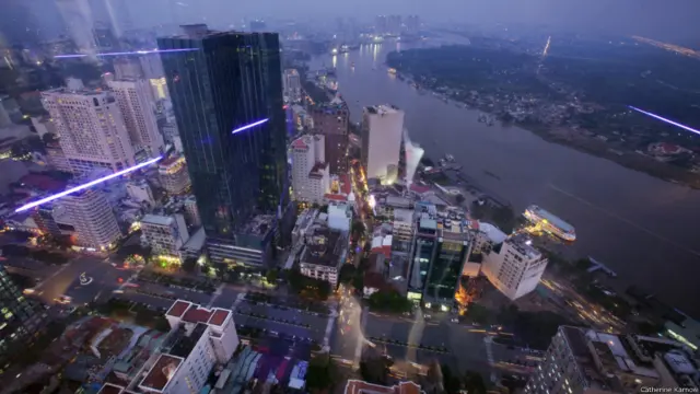 TP HỒ CHÍ MINH NHÌN TỪ THÁP BITEXCO, 2012. Nhìn từ toà nhà Bitexco 68 tầng, một trong những toà nhà cao nhất Việt Nam, cảnh vật TP Hồ Chí Minh thay đổi chóng mặt mỗi năm. Nơi xưa kia là những biệt thự Pháp xây dọc theo sông Sài Gòn, ngày nay có một đường hầm mới, hoàn thành vào năm 2011, nối liền trung tâm thành phố với các ngoại ô lân cận. Trong khi các toà nhà cao tầng mọc lên với tốc độ chóng mặt, tốc độ tăng trường kinh tế lại chậm hơn nên các không gian văn phòng luôn thiếu người thuê. 