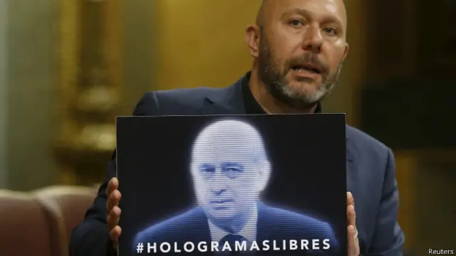 Un diputado de la oposición, sostiene un cartel del ministro de Interior español, Jorge Fernández Díaz, convertido en holograma.