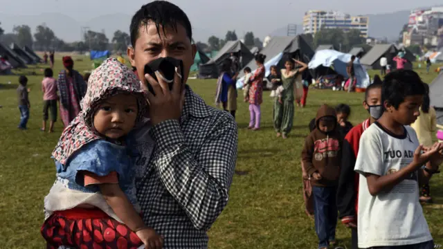 ایک شخص اپنے بچے کو گود میں اٹھائے بچوں کے کھانے پینے کے سامان کے لیے بنی قطار کو دیکھ رہا ہے۔