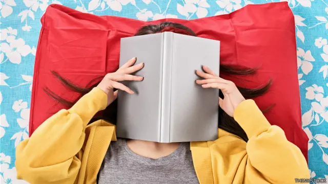 Chica acostada con libro tapándole la cara