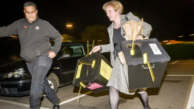 Petugas membawa dua kotak suara pertama dari kawasan pemilihan Bristol yang tiba di tempat penghitungan suara wilayah di City Academi Bristol.