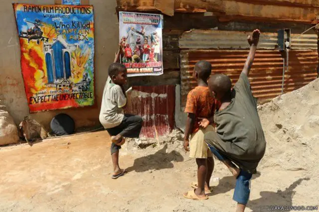 Anak-anak melakukan gerakan kung-fu di depan poster iklan film Wakaliwood
