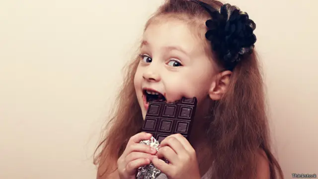 Niña con una barra de chocolate en la boca.