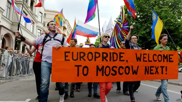 Люди с российскими и украинскими влагами в Риге несут оранжевый плакат с надписью: "Европрайд - добро пожаловать дальше в Москву"