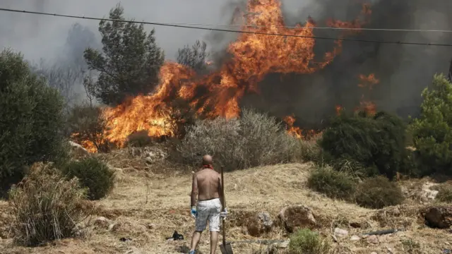 يوناني يتأمل ألسنة اللهب قرب منزله في ضاحية ليوبولي قرب العاصمة حيث دفعت الرياح النيران بسرعة وتسببت في انتشارها.