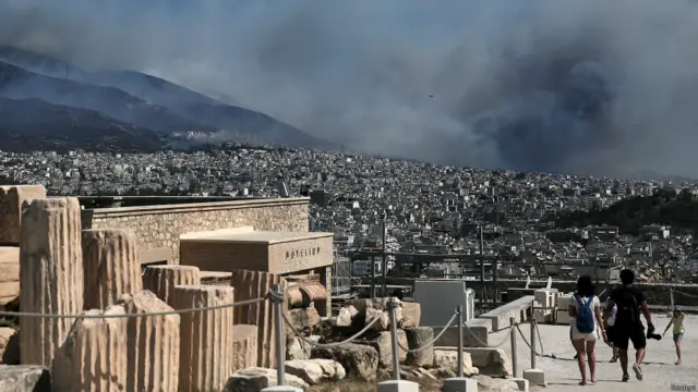 سائحون فوق تل أكروبوليس الأثري يراقبون سحب الدخان.