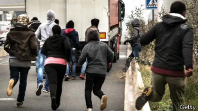 inmigrantes corriendo tras un camión que se dirige al Eurotúnel en Calais, Francia