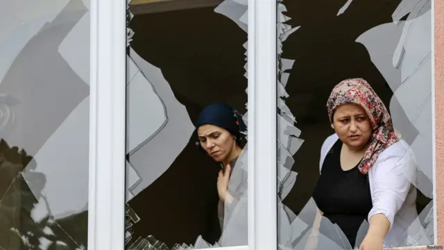 امرأة تنظر من نافذة تحطمت بعد الهجوم على مركز الشرطة القريب من منزلها في اسطنبول قتل فيه ثلاثة وأصيب عدد آخر