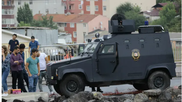 مجموعة من الأشخاص يقفون بالقرب من عربة مدرعة تابعة لقوات الشرطة الخاصة خارج مركز الشرطة الذي تعرض للهجوم في اسطنبول