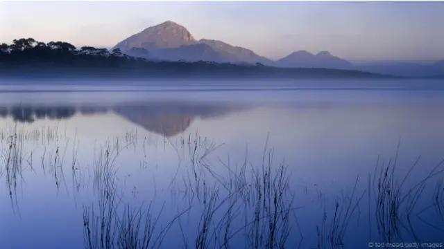 Mt Rugby soi bóng xuống vịnh Bathurst Harbour mờ sương (Hình: Ted Mead/Getty Images)