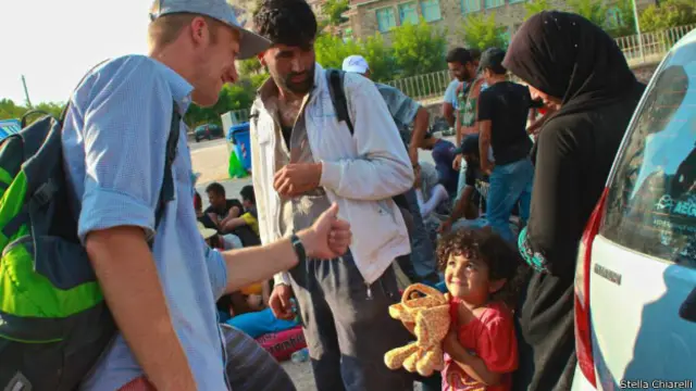 Voluntário dá brinquedo a criança refugiada, à espera do ônibus para Mytilene