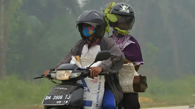 Warga Pekan Baru melintas di sebuah jalan yang dipenuhi kabut asap akibat pembakaran hutan dan lahan.