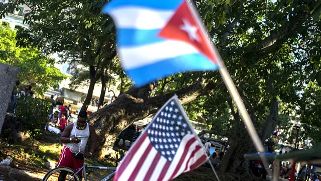 一男子站于哈瓦那街头古巴与美国国旗后面