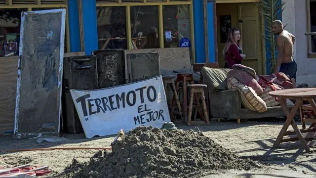 Vecinos de la localidad de Tongoy, una zona de playa a 400 km de Santiago de Chile, sacan muebles de su vivenda al lado del cartel que promociona una bebida local apodada "terremoto".
