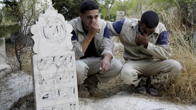 عنصران من الدفاع المدني السوري يبكيان بحانب قبر زميل لهما يقول ناشطون إنه قتل في غارة روسية في ريف إدلب.