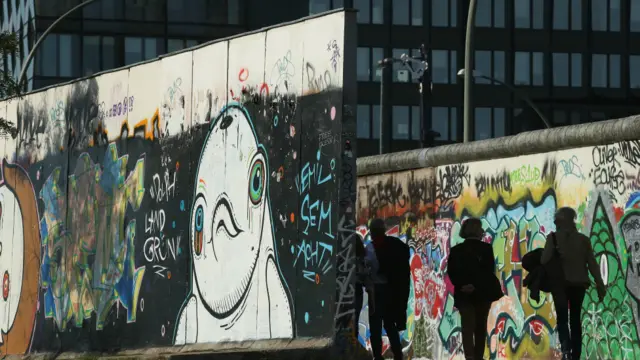 Orang-orang berjalan di bagian Tembok Berlin di Galeri Sisi Timur sehari sebelum perayaan 25 tahun penyatuan Jerman. 