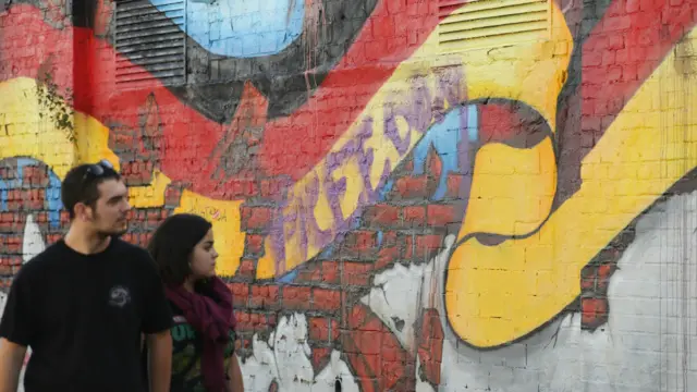 Orang-orang berjalan di depan mural yang menunjukkan bendera Jerman sehari sebelum peringatan 25 tahun penyatuan Jerman di Berlin. 