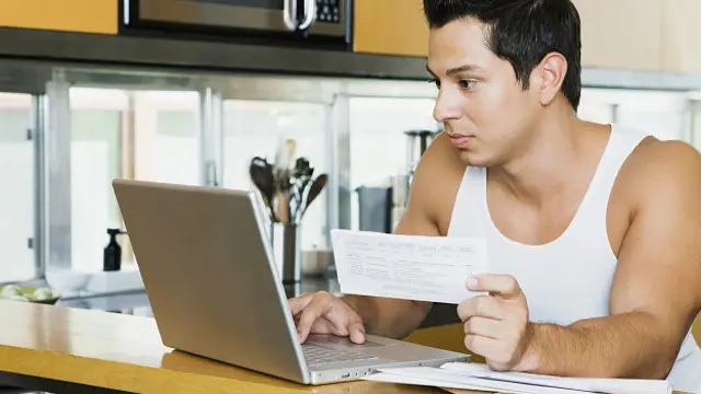 Мужчина проверяет свой счет онлайн, сидя на кухне