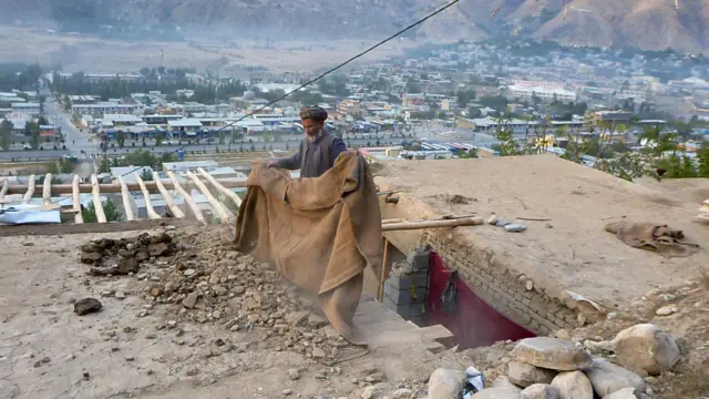 أفغاني يزيل الدمار فوق سقف منزله، أفغانستان.