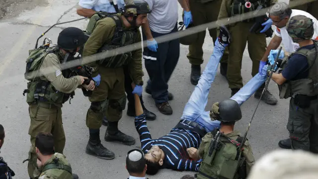 جنود إسرائيليون بجانب فلسطيني مصاب في مدينة الخليل بالضفة الغربية. 