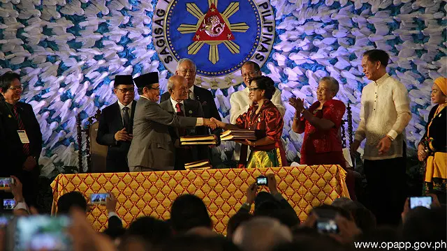 محقر اقبال (چپ) مذاکره کننده ارشد ام آی ال اف و مریم کرونل-فرر، نماینده ارشد دولت فیلیپین در حال دست دادن پس از امضای توافقنامه جامع 'بنگسامورو' در مانیل.
این توافقنامه پس از ۱۷ سال مذاکرات پی هم برای پایان یک جنگ ۴۰ ساله به امضا رسید 