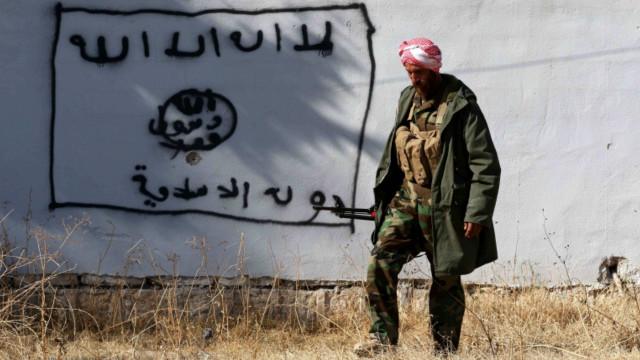 Курдский военный идет мимо граффити с символами ИГ в Синджаре