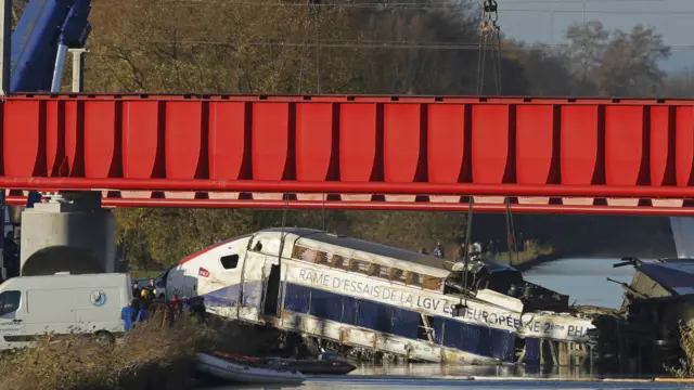 工作人员使用吊车试图将事故列车从水中脱出。