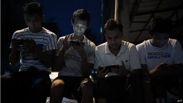 Anak muda menatap layar telepon seluler pada malam hari dalam keadaan gelap.